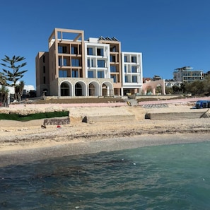 A modern multi-story building with a flat roof, large windows, and a stone base. - Hotel Camelot By Artur (Ksamil)
