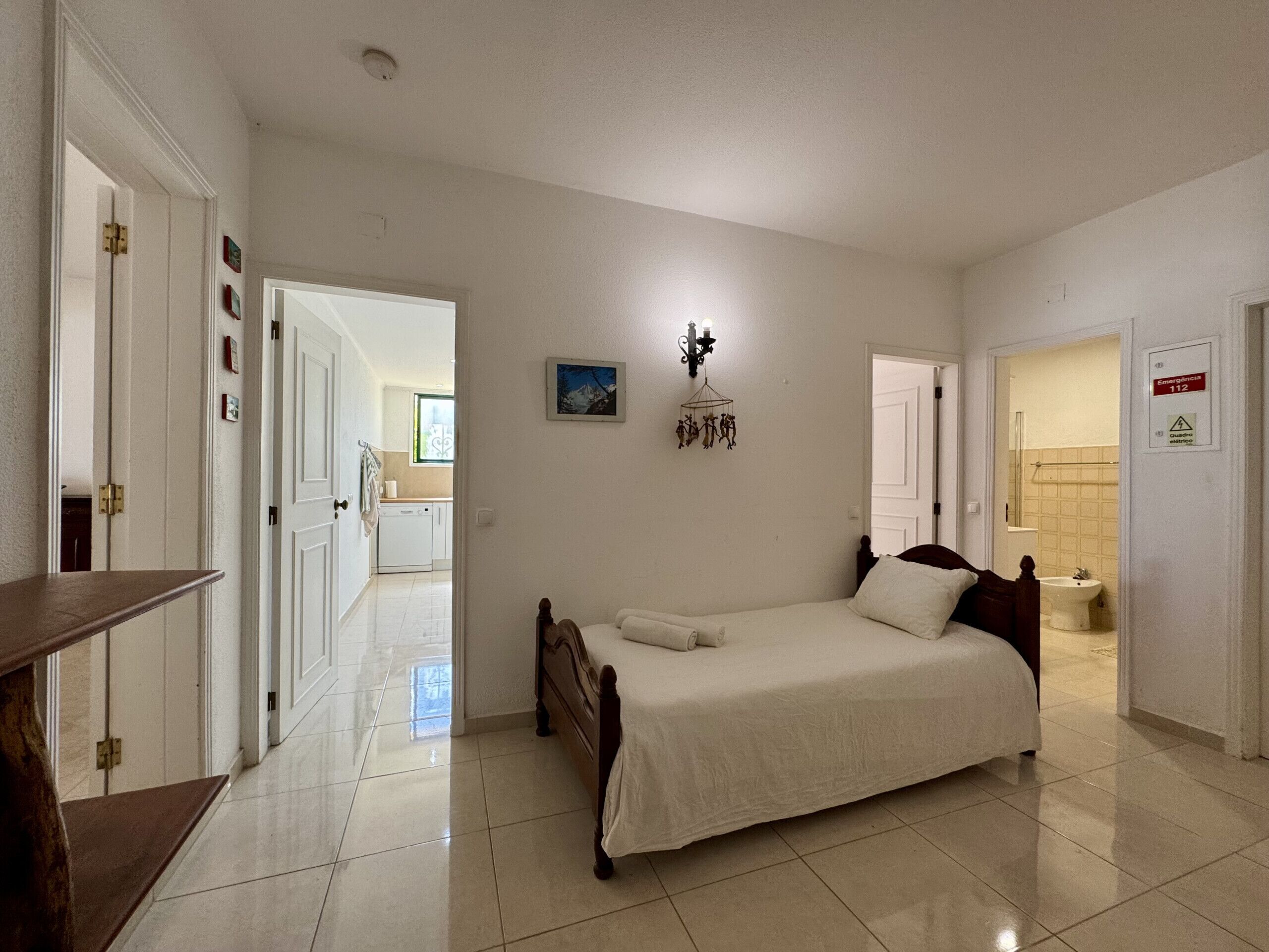 Un dormitorio con cama, mesita de noche, lámpara de pared y puerta que da al baño.