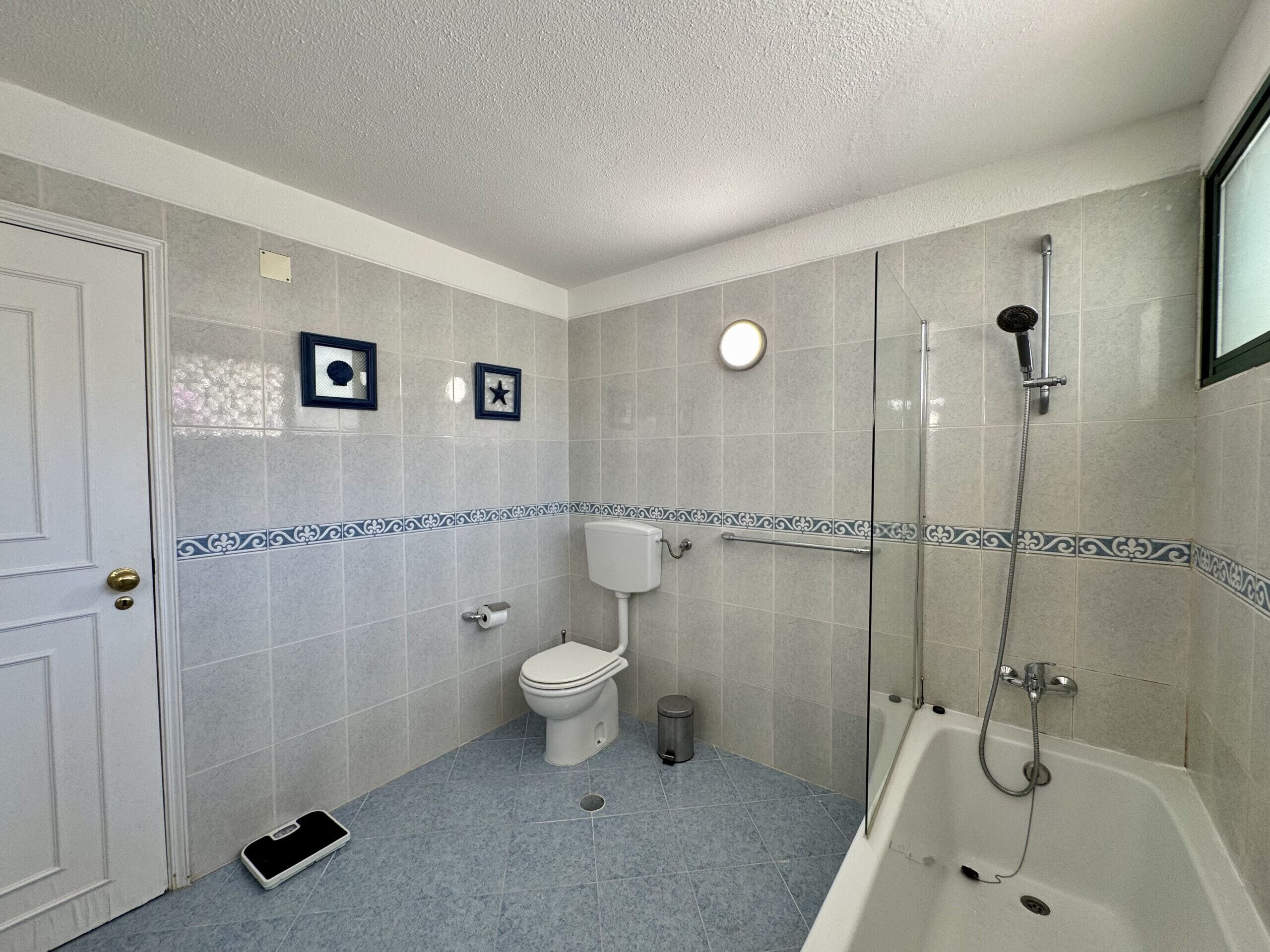 A bathroom with a toilet, bidet, and bathtub, featuring a tiled floor and walls with a decorative border.