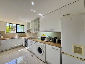 Eine moderne Küche mit weißen Schränken, einer Waschmaschine, einer Mikrowelle und einem Spülbecken.