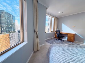 A hotel room with a bed, a desk, and a view of a cityscape. - Iconic Harbour Views at Quay West Sydney (The Rocks)