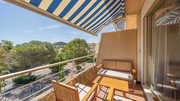 A balcony with a striped awning, wooden furniture, and a view of the surrounding area.