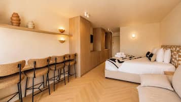 Habitación de hotel con cama, zona de estar con sillas, armario y cabina de ducha.