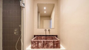 Ein Badezimmer mit einem rechteckigen Waschbecken, einem Spiegel darüber und einem Duschbereich mit einer gefliesten Wand.