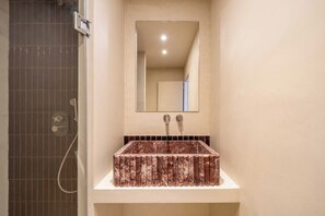 Ein Badezimmer mit einem rechteckigen Waschbecken, einem Spiegel darüber und einem Duschbereich mit einer gefliesten Wand.