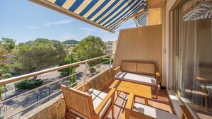 Ein Balkon mit Holzmöbeln, einem gestreiften Sonnenschirm und Blick auf die Straße und Grünflächen.