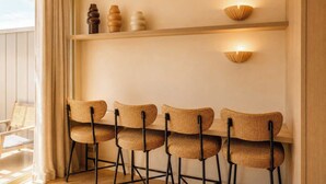 Ein Essbereich mit vier Korbstühlen, einem Holztisch und Wandleuchten.