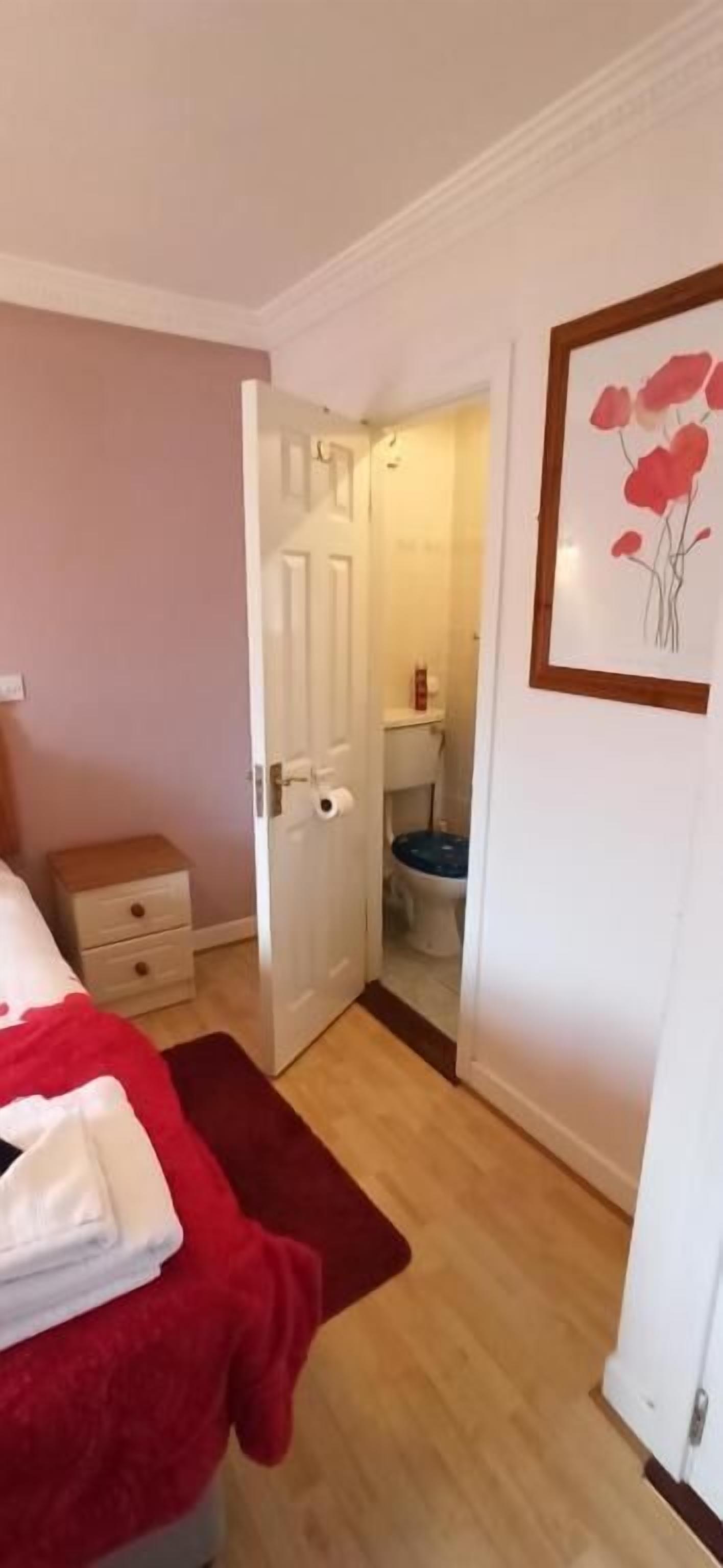 Une chambre à coucher avec un lit, une couverture rouge, une table de chevet et une porte donnant sur une salle de bain.