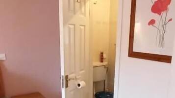 Une chambre à coucher avec un lit, une couverture rouge, une table de chevet et une porte donnant sur une salle de bain.