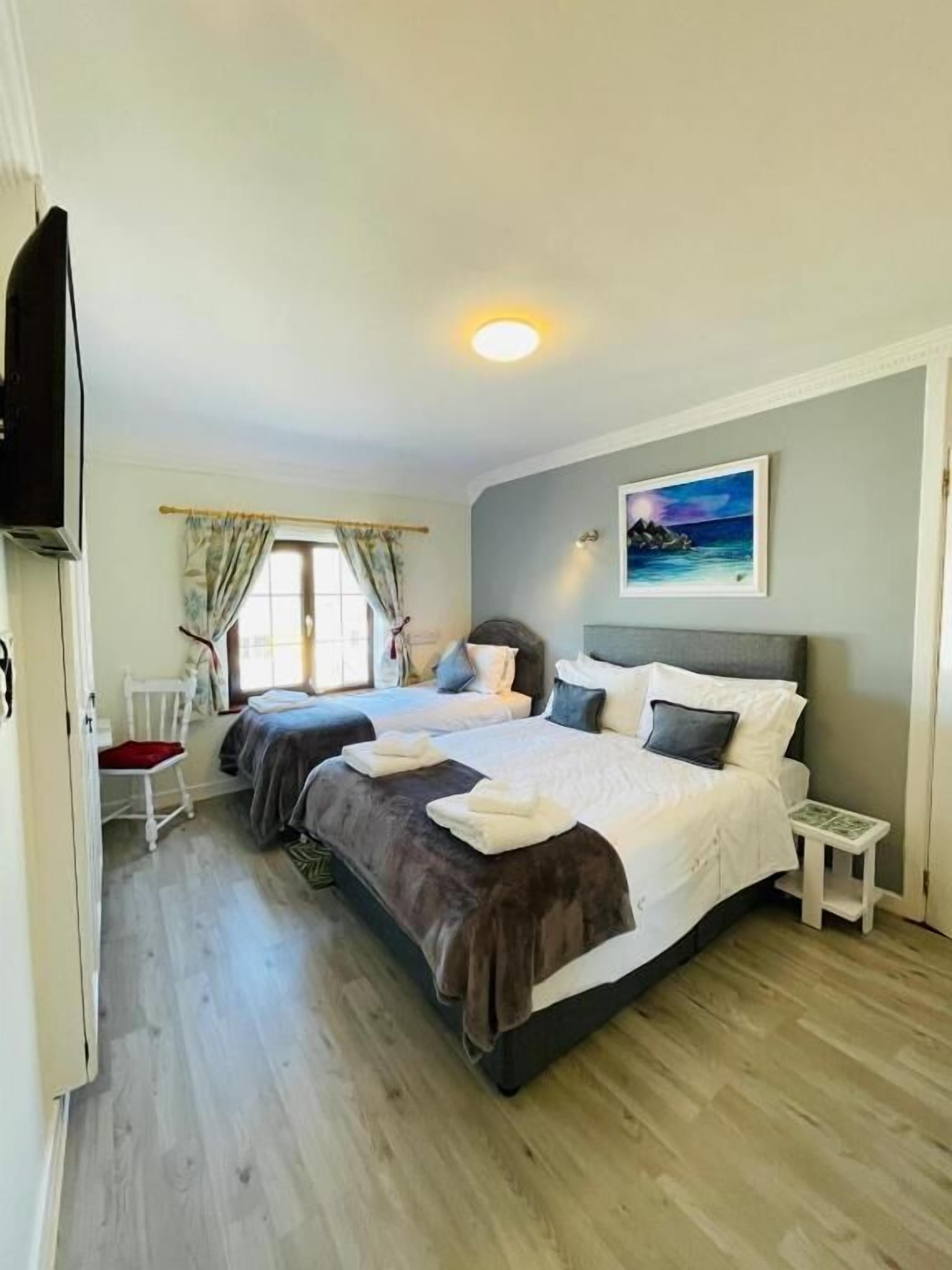 Quarto com duas camas, uma mesa pequena, uma cadeira e um quadro na parede.