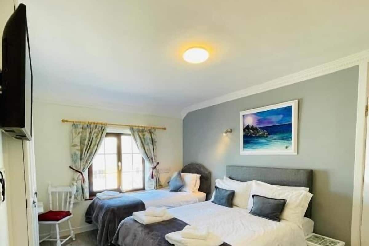 A bedroom with two beds, a small table, a chair, and a painting on the wall.