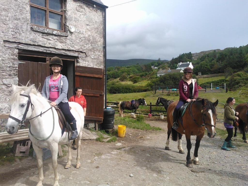 A rustic stone building with a wooden door, a dirt path, and horses.