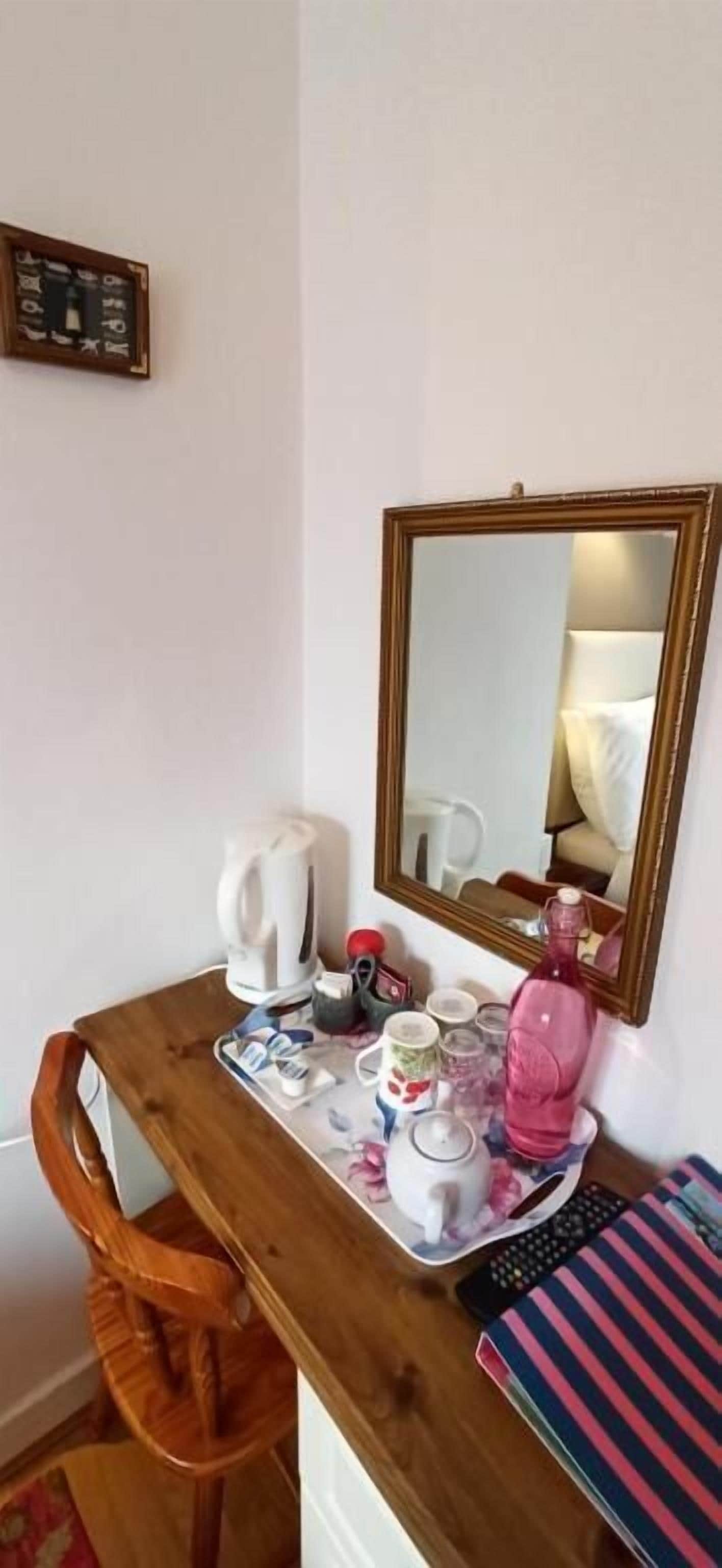 A wooden desk with a mirror, a kettle, a pink bottle, and a striped towel.