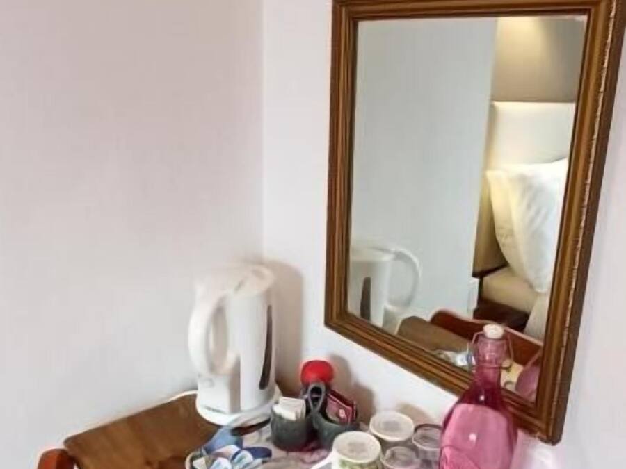 A wooden desk with a mirror, a kettle, a pink bottle, and a striped towel.