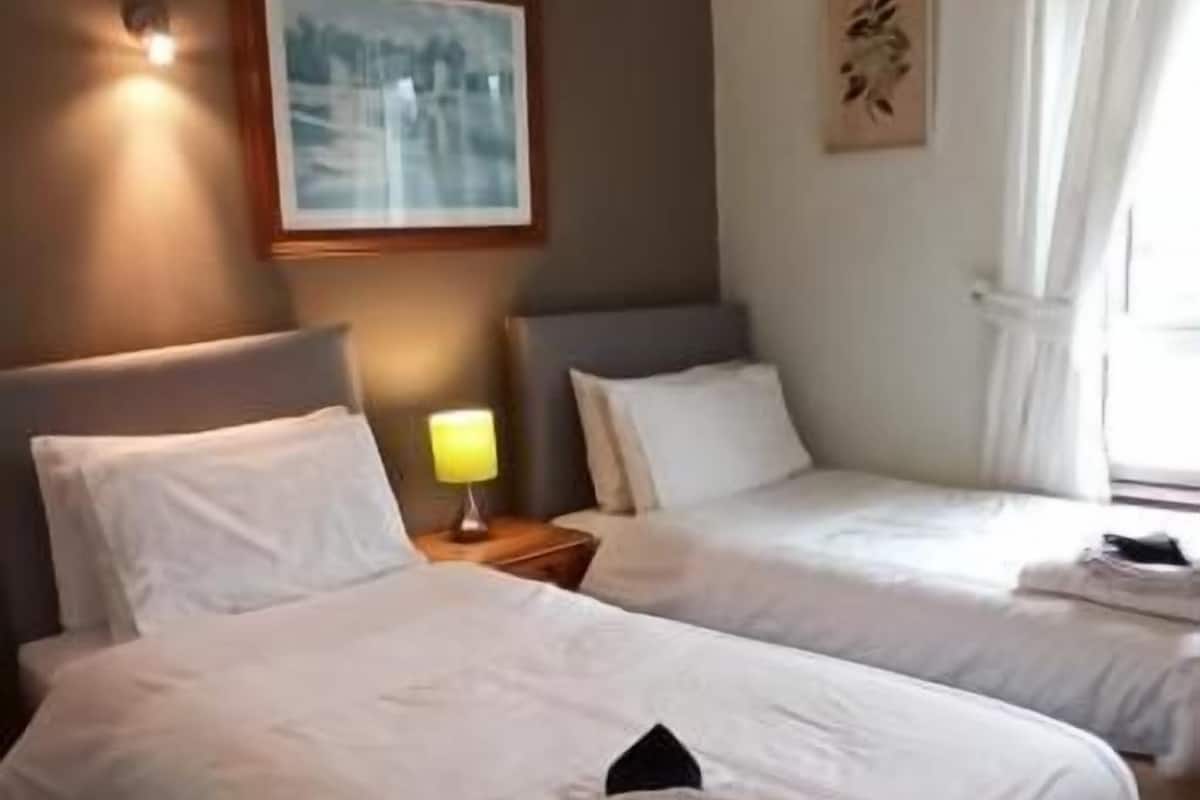 A hotel room with two beds, a nightstand with a lamp, a framed picture on the wall, and a window with curtains.