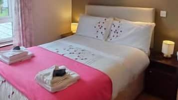 Una cama bien tendida con una manta rosa, una mesita de noche con una lámpara y una alfombra estampada.