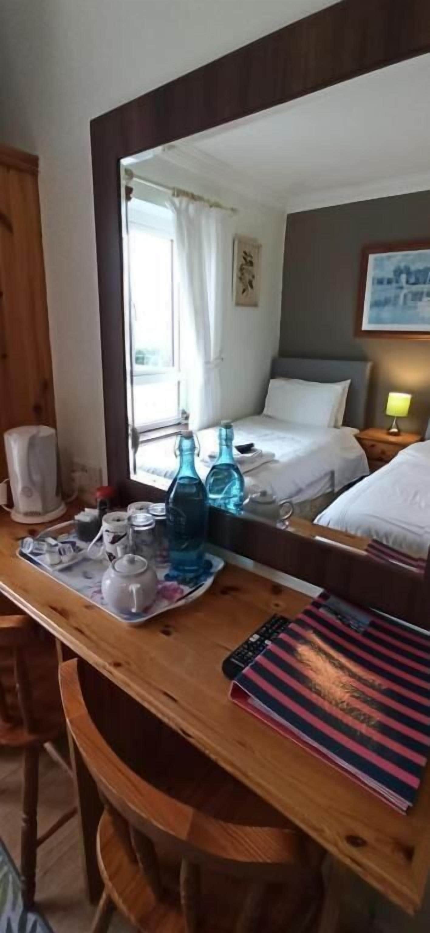 A hotel room with a wooden desk, a bed, a nightstand, a mirror, and a window with curtains.