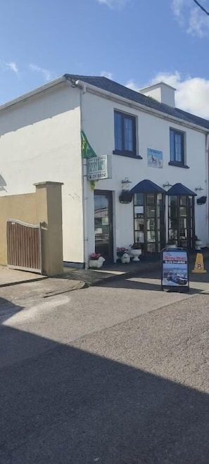 A building with a signboard, a gated entrance, and a small outdoor seating area. - The Ferry Boat (Portmagee)