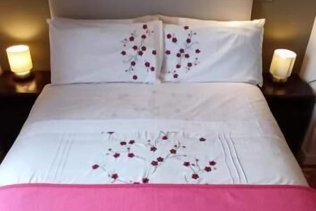 A neatly made bed with white linens and pink bedspread, two white towels on the bed, and bedside lamps on either side.