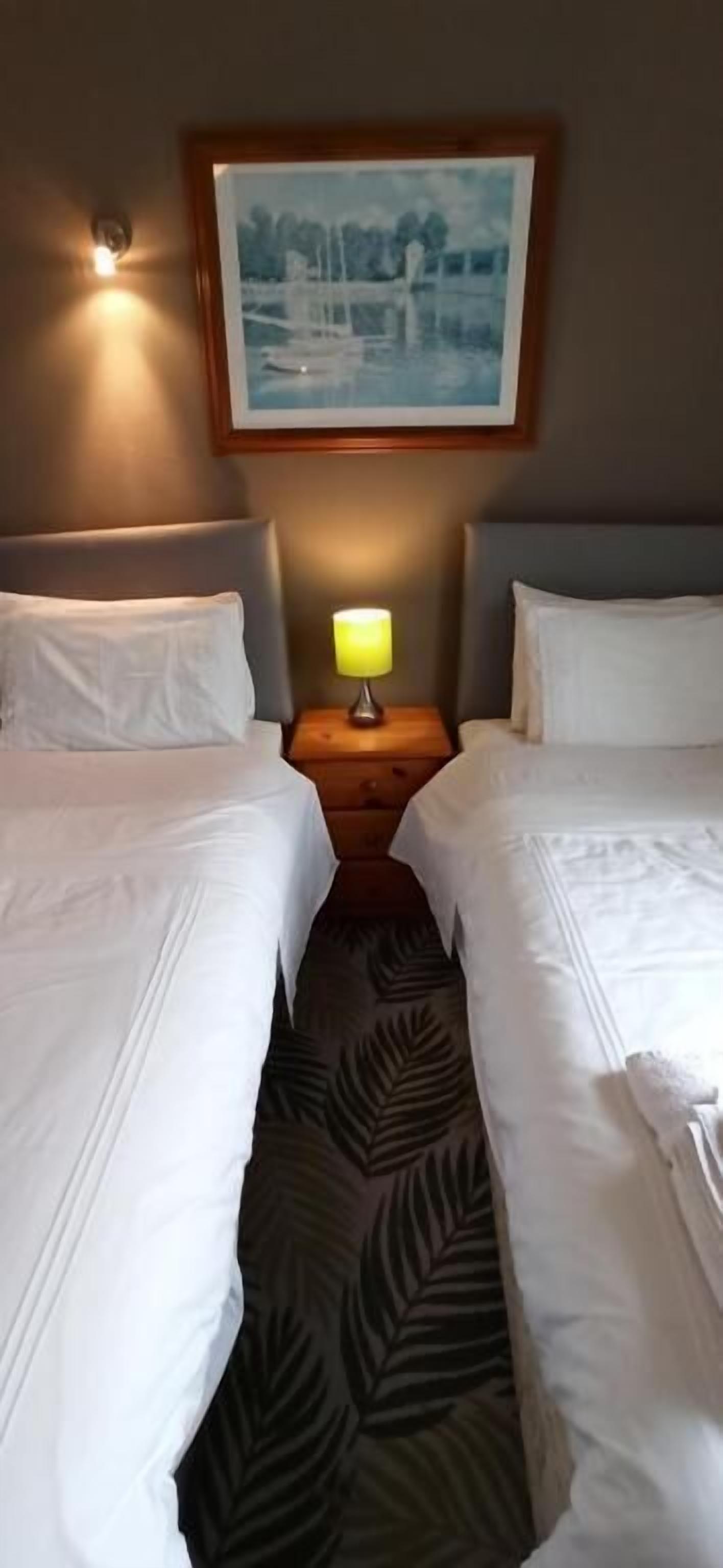 A hotel room with two beds, a nightstand with a lamp, a framed picture on the wall, and a patterned carpet.