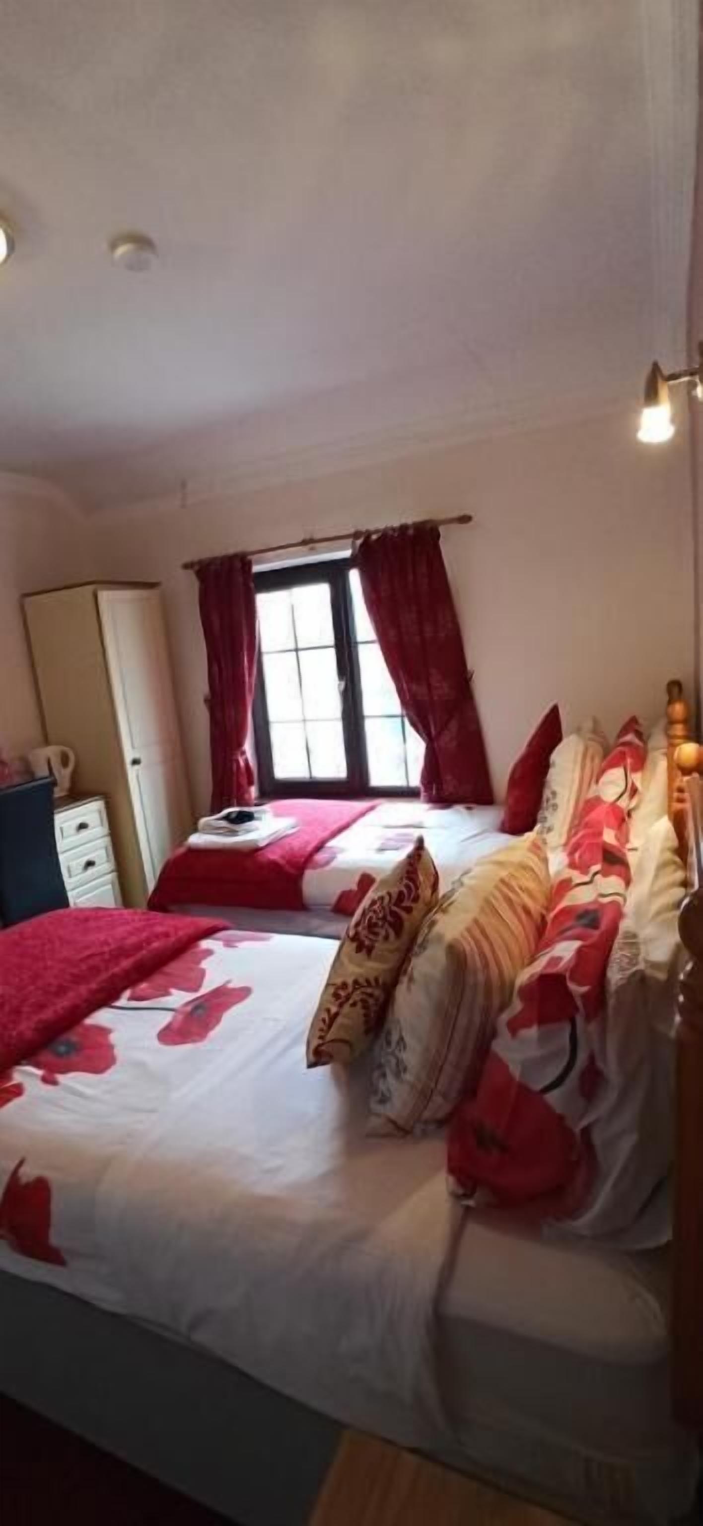 Quarto com duas camas, janela com cortinas, guarda-roupa e mesa de cabeceira.