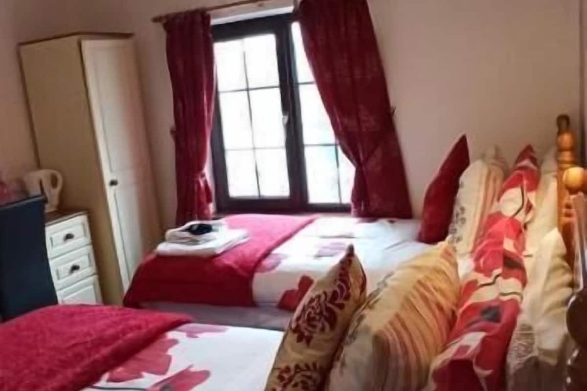 A bedroom with two beds, a window with curtains, a wardrobe, and a bedside table.