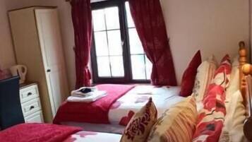 Un dormitorio con dos camas, una ventana con cortinas, un armario y una mesita de noche.