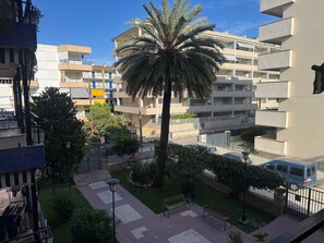 Un edificio residencial con varios balcones, una palmera y un patio empedrado con bancos.