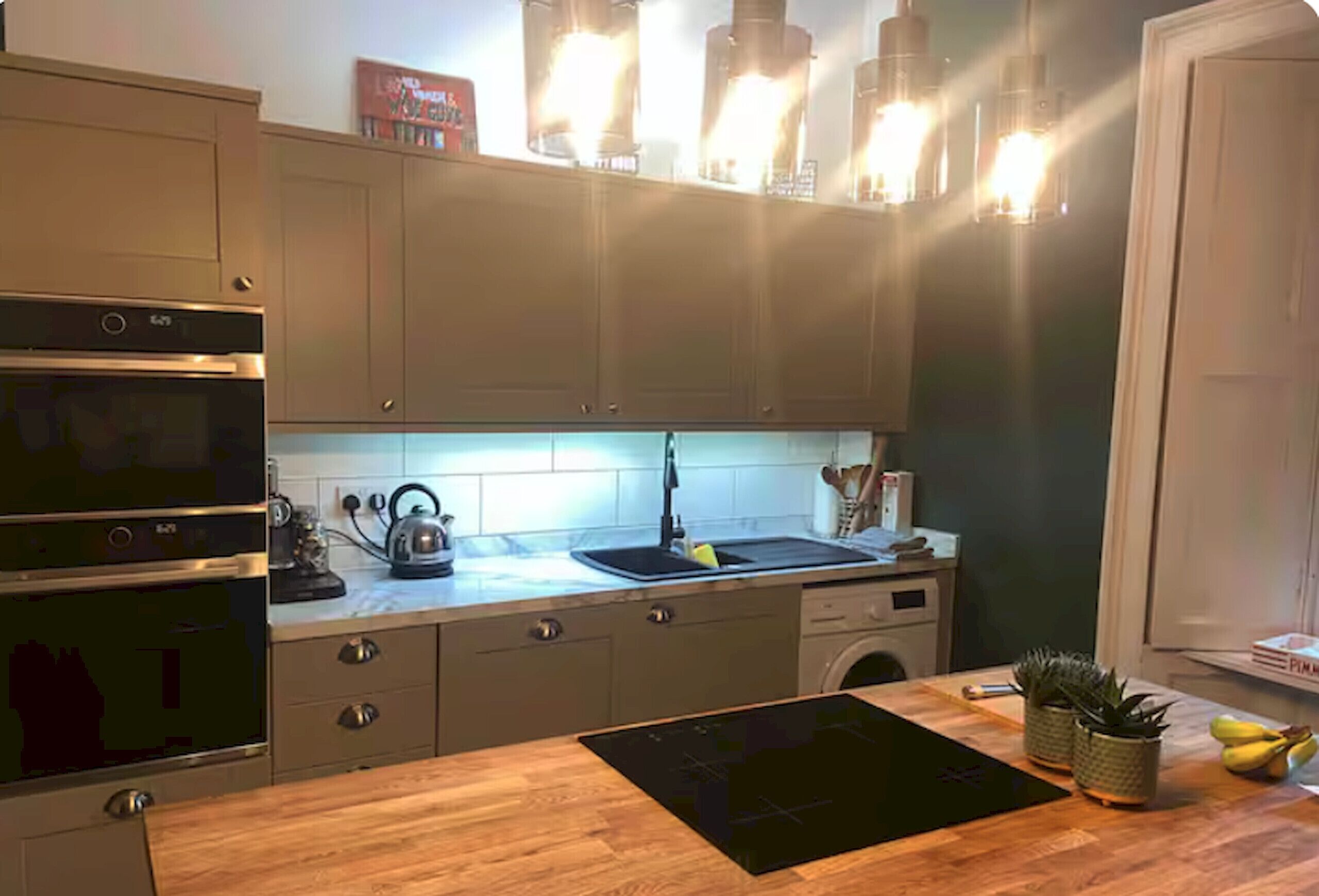 Une cuisine dotée d’un plan de travail en bois, d’appareils électroménagers en acier inoxydable et de luminaires suspendus.
