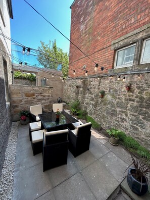 A patio with outdoor furniture, a stone wall, and a brick building in the background. - Greyfriars Garden No (14A) | St Andrews (St Andrews)