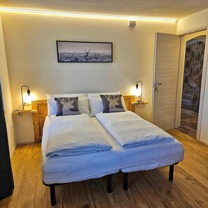 Un letto matrimoniale con due cuscini, un comodino con una lampada, un quadro appeso al muro e un pavimento in legno.