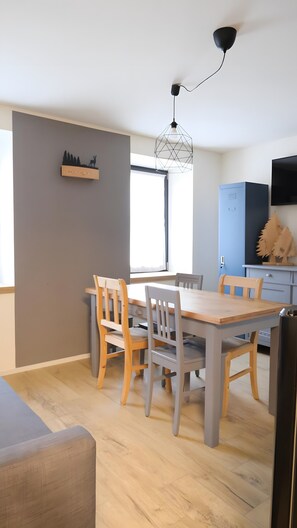 Zona pranzo con tavolo e sedie in legno, una lampada a sospensione, uno scaffale a parete con decorazione a silhouette e una finestra che lascia entrare luce naturale.