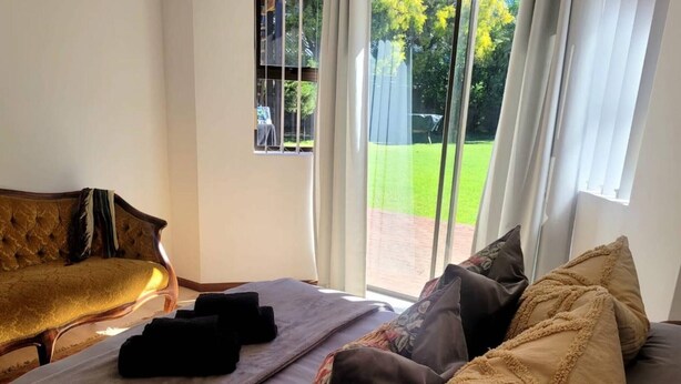 A bedroom with a bed, a sofa, and a window with curtains. - Elegant Two-bedroom Apartment on the Banks of the Eerste River in Stellenbosch (Stellenbosch)
