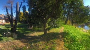 A pathway leading to a building with a brick facade, surrounded by trees and a fence. - Elegant Two-bedroom Apartment on the Banks of the Eerste River in Stellenbosch (Stellenbosch)