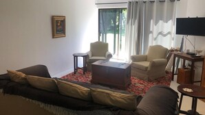 A living room with a sofa, chairs, a coffee table, a painting, and a TV. - Elegant Two-bedroom Apartment on the Banks of the Eerste River in Stellenbosch (Stellenbosch)