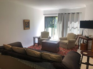 Uma sala de estar com sofá, cadeiras, mesa de centro, quadro e televisão.