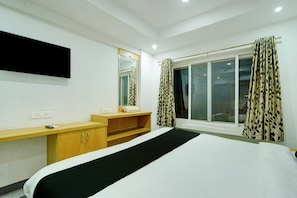A hotel room with a bed, a wooden desk, a mirror, a television mounted on the wall, and a window with curtains. - Classic Room With Twin Bed Hotel Looranova (Tirupati)
