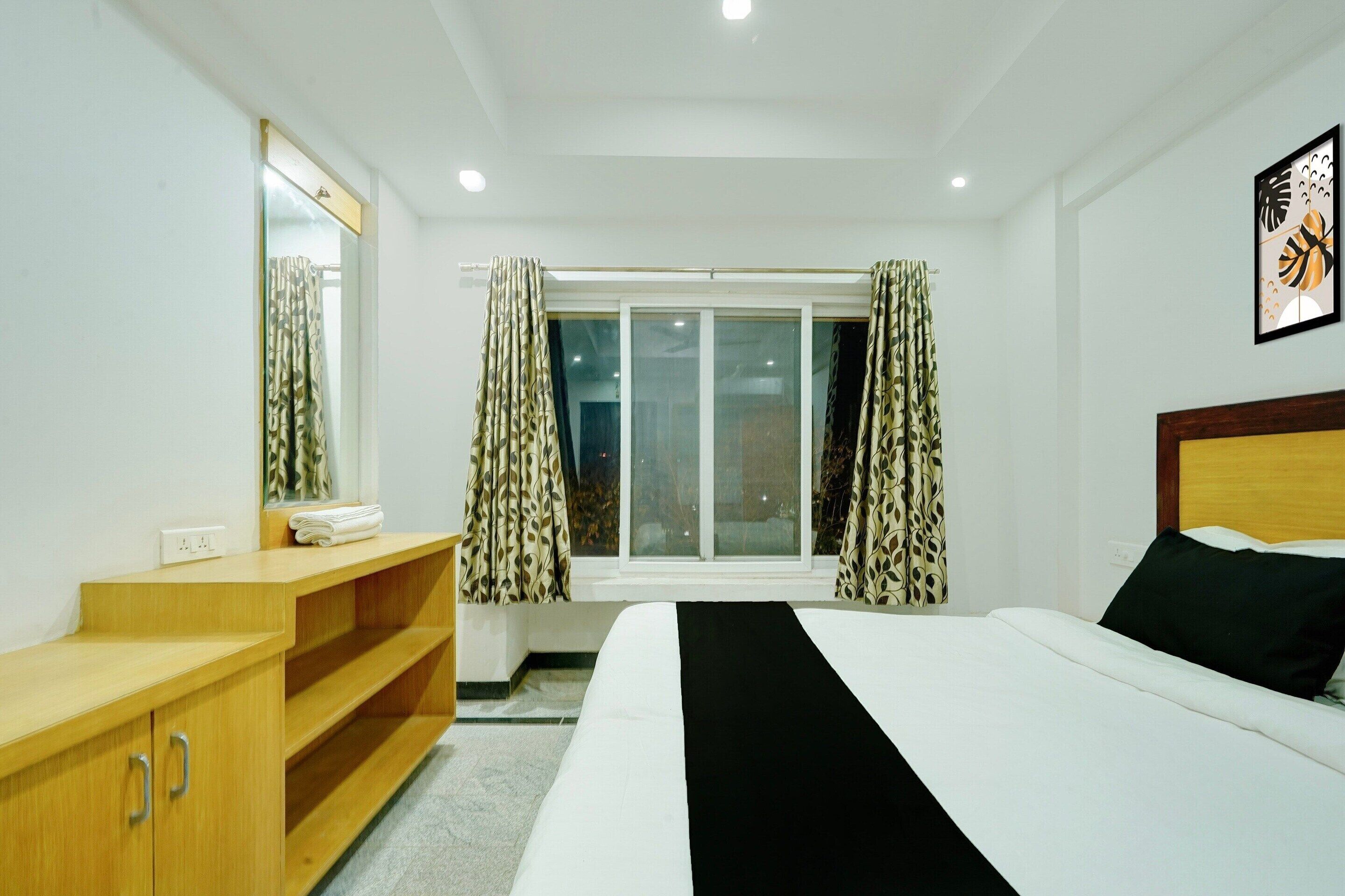 Ein Hotelzimmer mit einem Bett, einem Holzkapständer, einem Fenster mit Vorhängen und einem Wandbild.