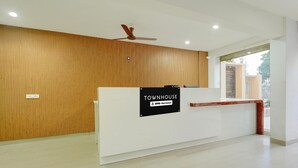 A reception desk with a sign reading 'TOWNHOUSE OYO-Serviced,' a ceiling fan, and a window with a view. - Classic Room With Twin Bed Hotel Looranova (Tirupati)
