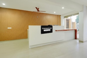 A reception desk with a sign reading 'TOWNHOUSE OYO-Serviced,' a ceiling fan, and a window with a view. - Classic Room With Twin Bed Hotel Looranova (Tirupati)