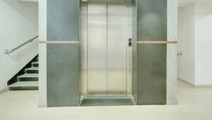 An elevator with a metallic finish, flanked by walls with a textured pattern, and a staircase to the left. - Classic Room With Twin Bed Hotel Looranova (Tirupati)