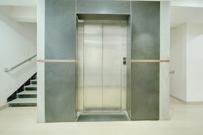 An elevator with a metallic finish, flanked by walls with a textured pattern, and a staircase to the left. - Classic Room With Twin Bed Hotel Looranova (Tirupati)