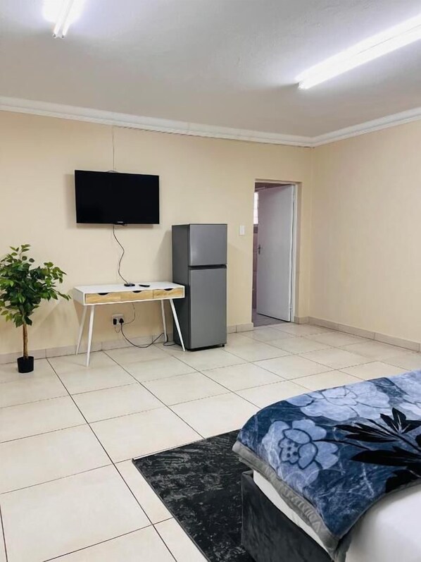 A bedroom with a bed, a desk, a television, and a refrigerator. - Room-airport Continental Guest House (Kempton Park)