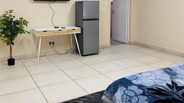 A bedroom with a bed, a desk, a television, and a refrigerator. - Room-airport Continental Guest House (Kempton Park)
