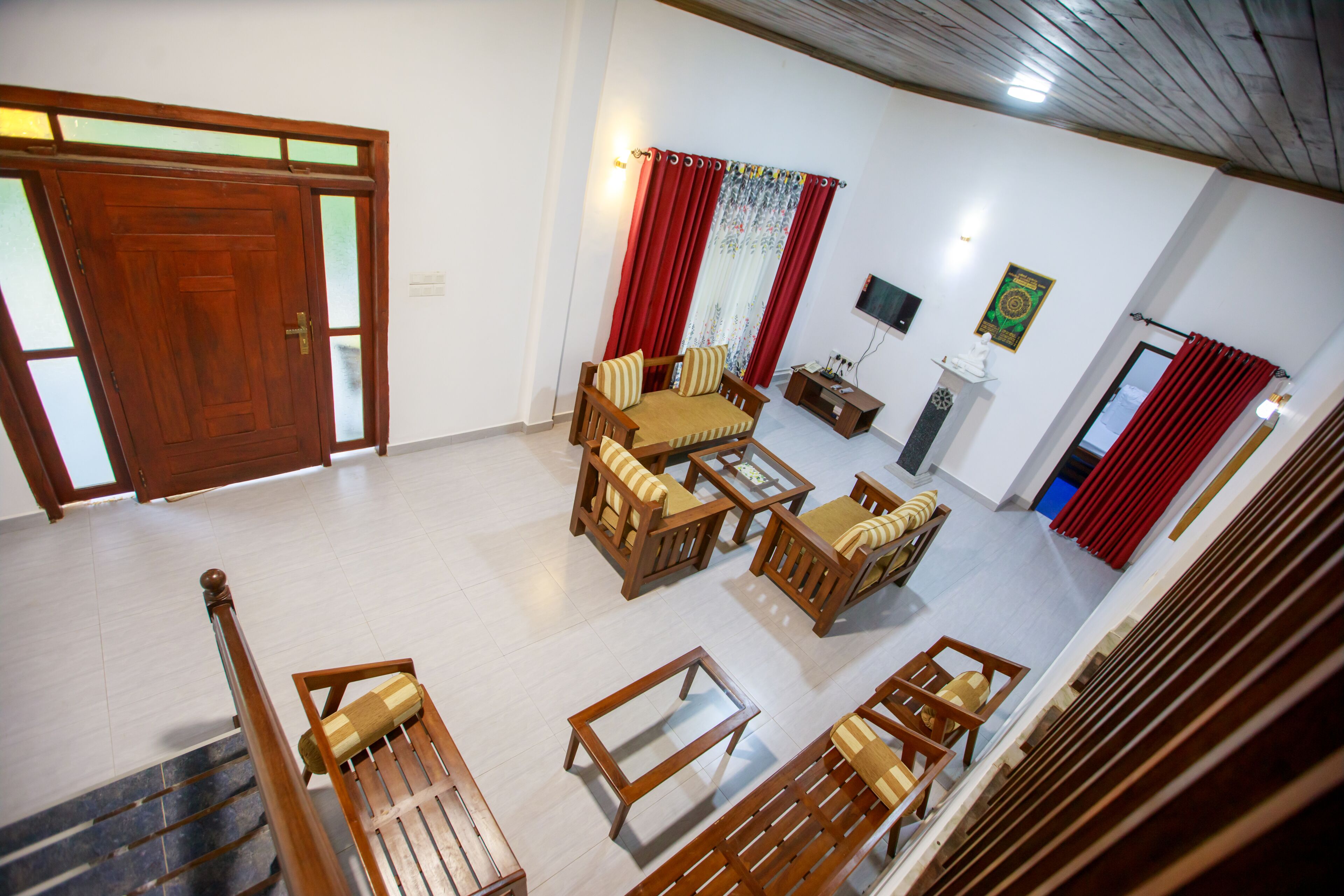 A spacious living area with a wooden staircase, a sofa set, a television, and a decorative wall piece.