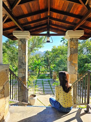 A covered outdoor area with stone pillars, a wooden ceiling, and a view of lush greenery. - Meadow Villa - Ella (Ella)