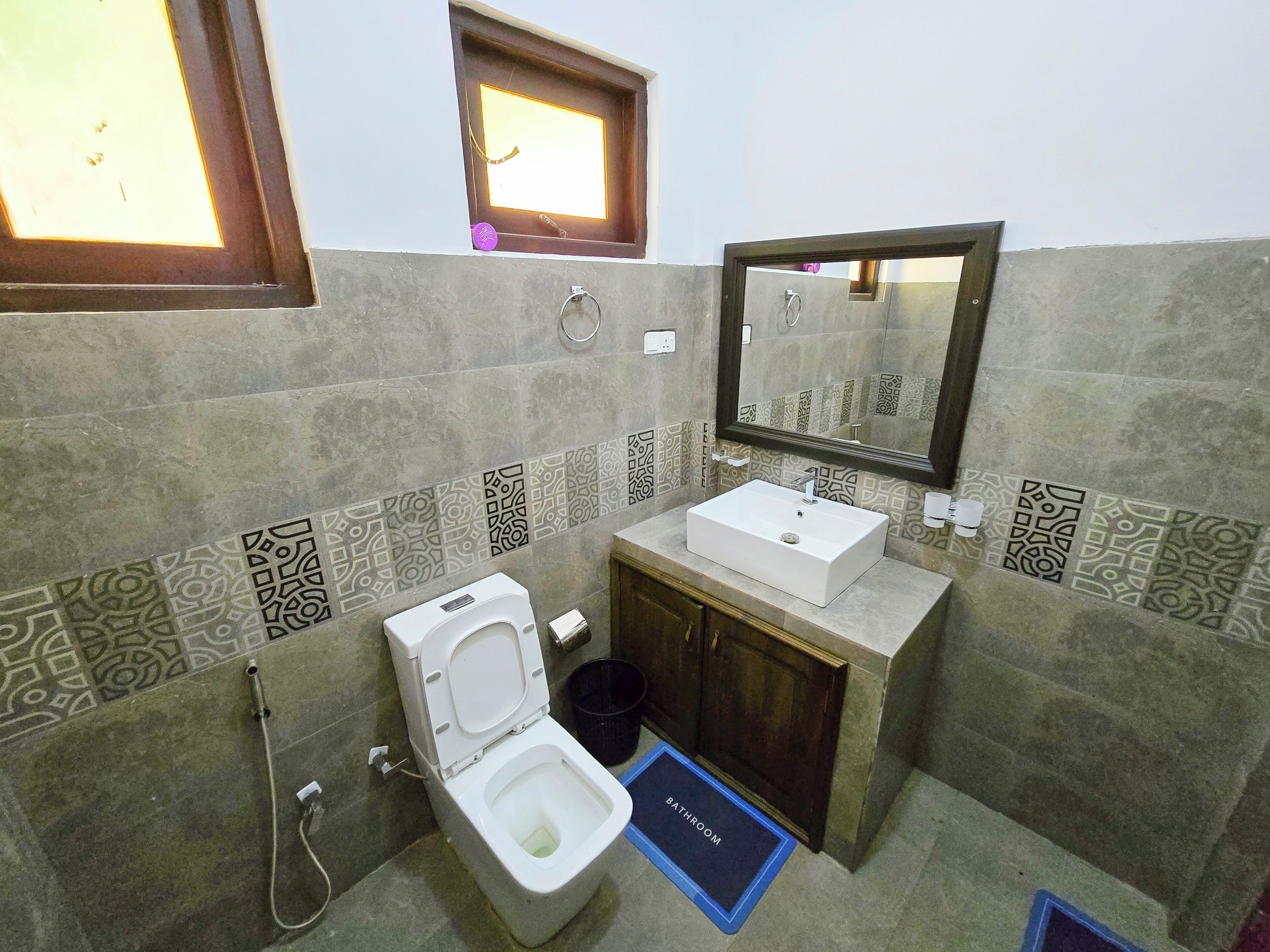 A bathroom with a toilet, sink, mirror, and patterned tiles.