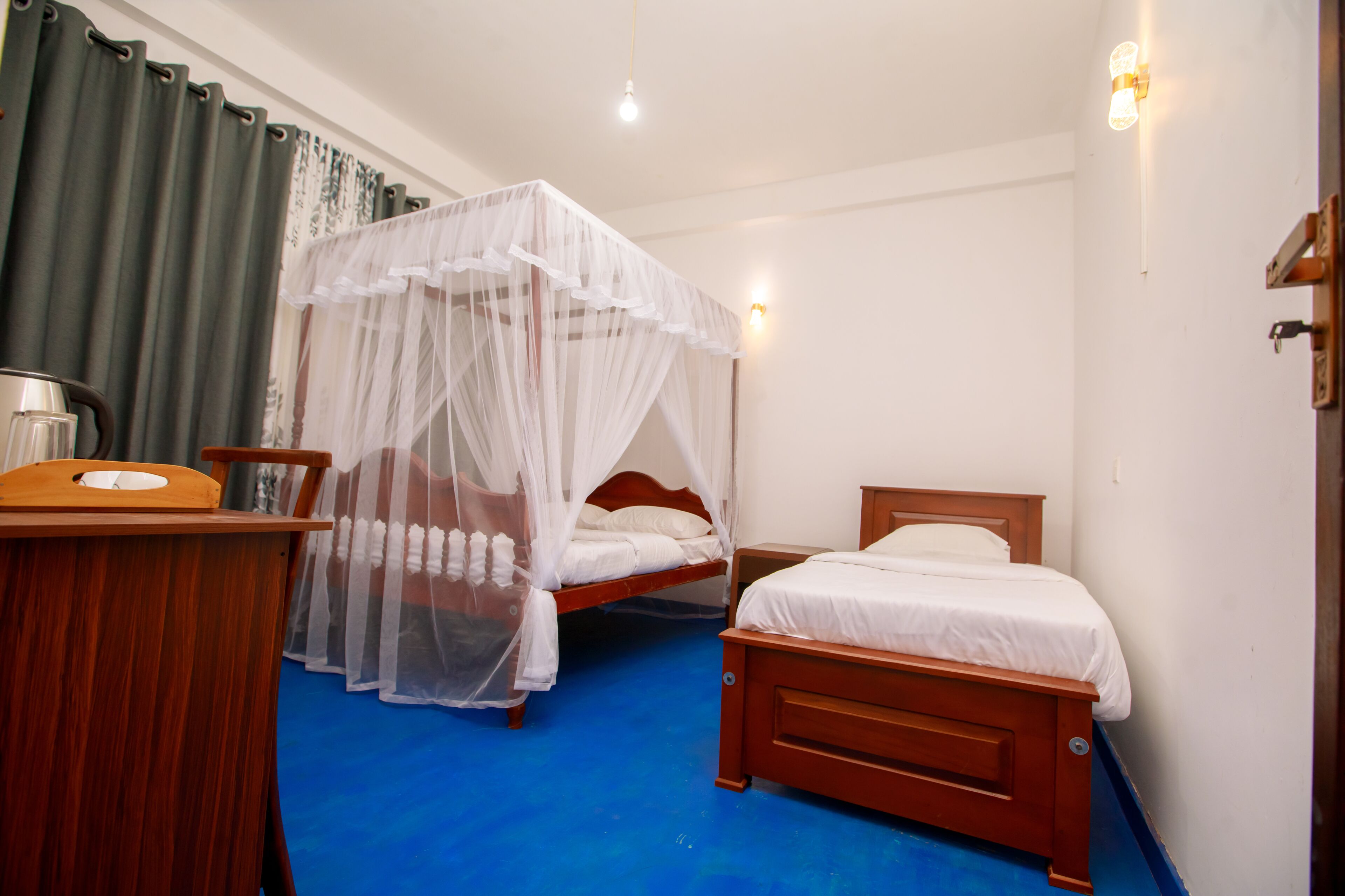 A bedroom with a canopy bed, a single bed, a desk with a chair, and a bedside table.