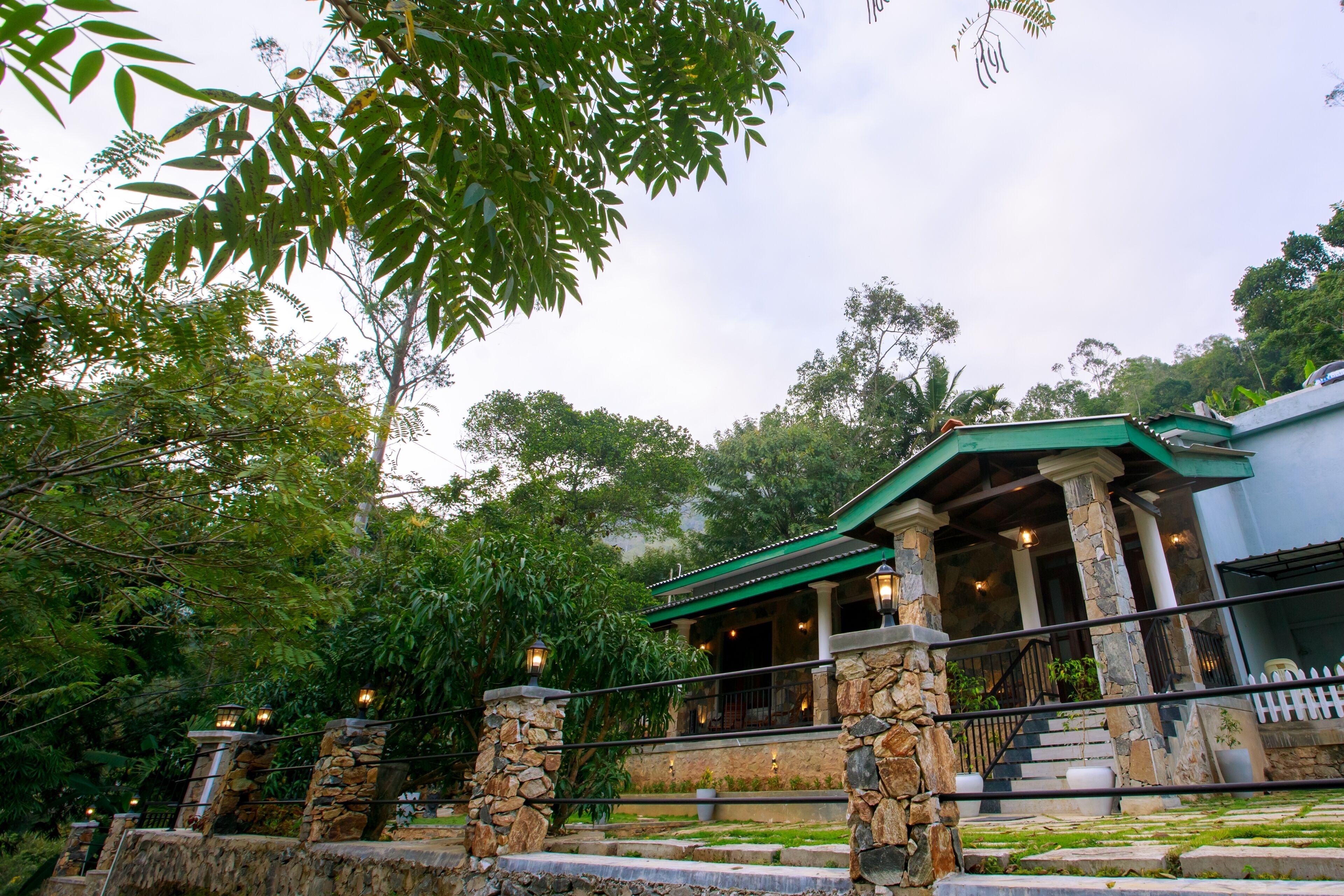 A stone-walled building with a green roof, columns, and a staircase leading to a porch.
