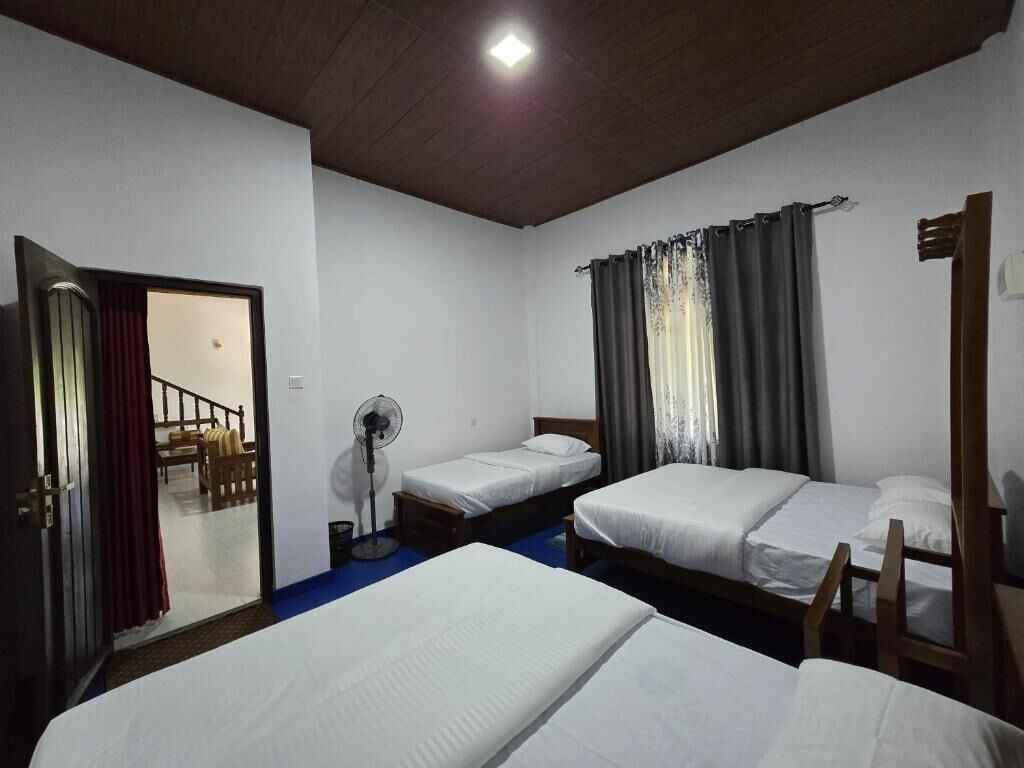 A room with three single beds, a standing fan, and a wooden chair.